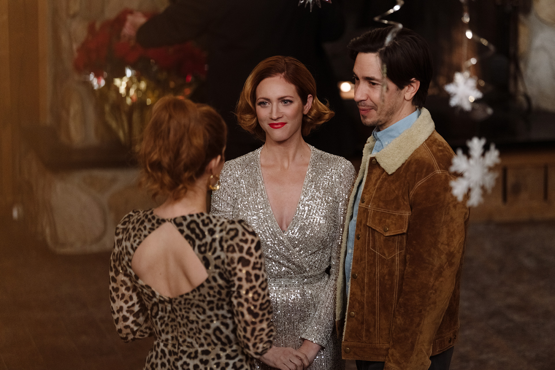 CHRISTMAS WITH THE CAMPBELLS film still featuring Brittney Snow and Justin Long listening to another character with back turned to us.