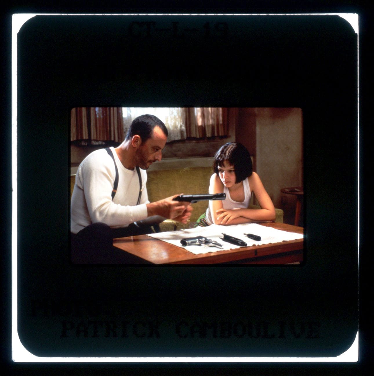 Color publicity slide from THE PROFESSIONAL featuring Jean Reno and Natalie Portman sitting at a table while he teaches her how to clean and reassemble his gun.