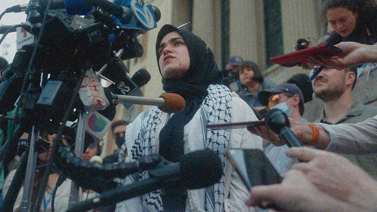 Sueda Polat conducting a press conference in front of a collection of microphones and cameras.