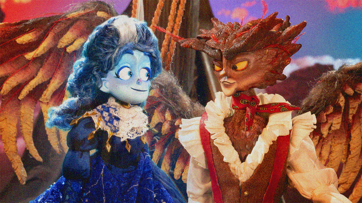 Stop-motion puppets: a woman in blue with a white streak in her hair smiles at an owl-man dressed in frills who's smiling back.