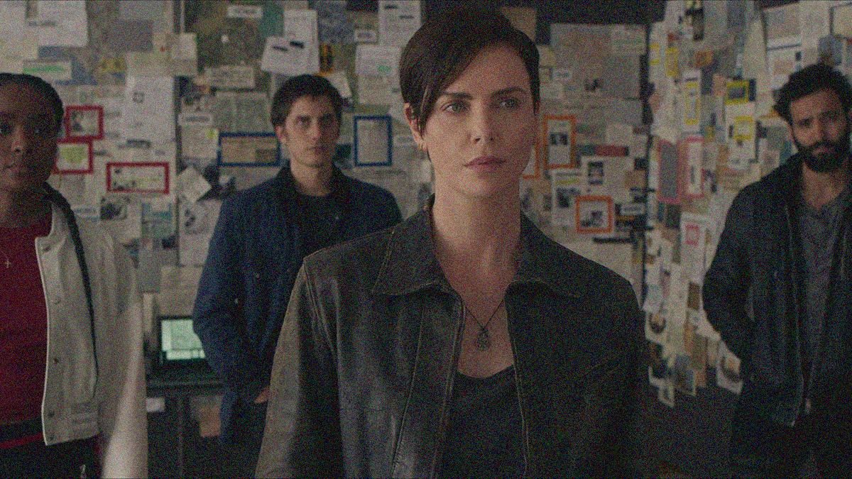 Two women and two men looking at the camera and blocked so all are visible against a wall of news clippings and photos piecing together a puzzle.