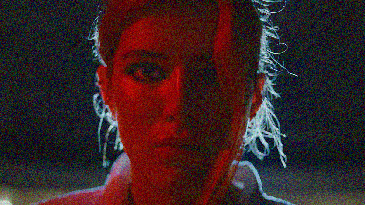 Bella Thorne in close-up at night under a filter of red light, staring intently into the camera.