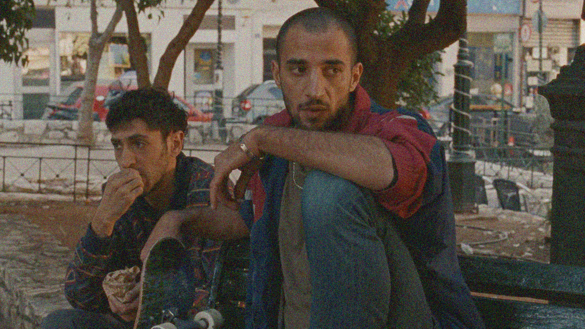 Aram Sabbah (eating) and Mahmoud Bakri (scoping out the area out of frame) sit on a park bench.