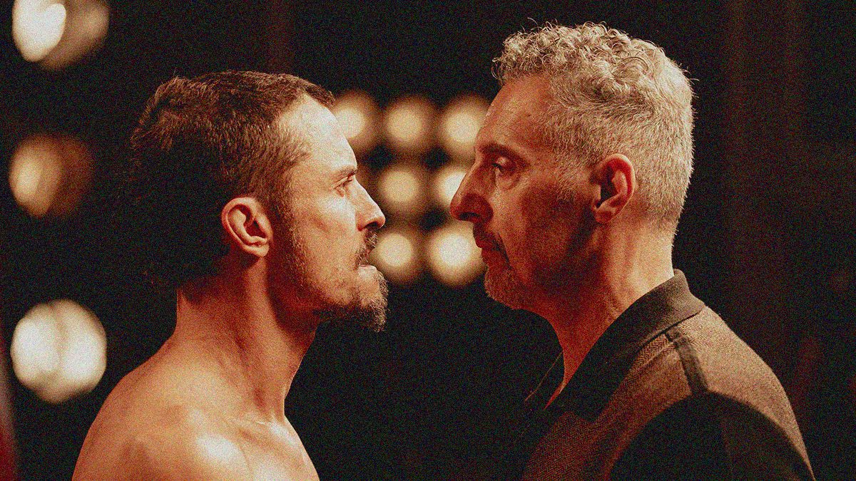 Two men in profile staring at each other with bright lights in the background.