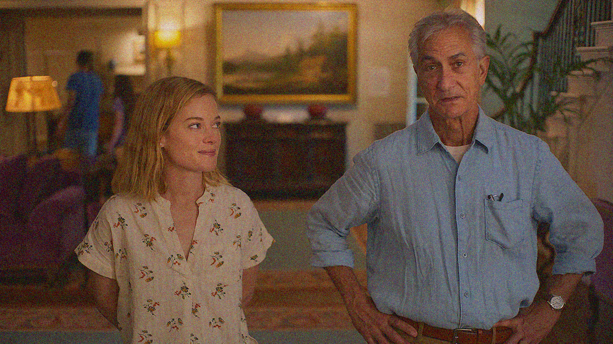 A woman stands smiling and looking at the older man next to her, he's looking forward with hands on hips.
