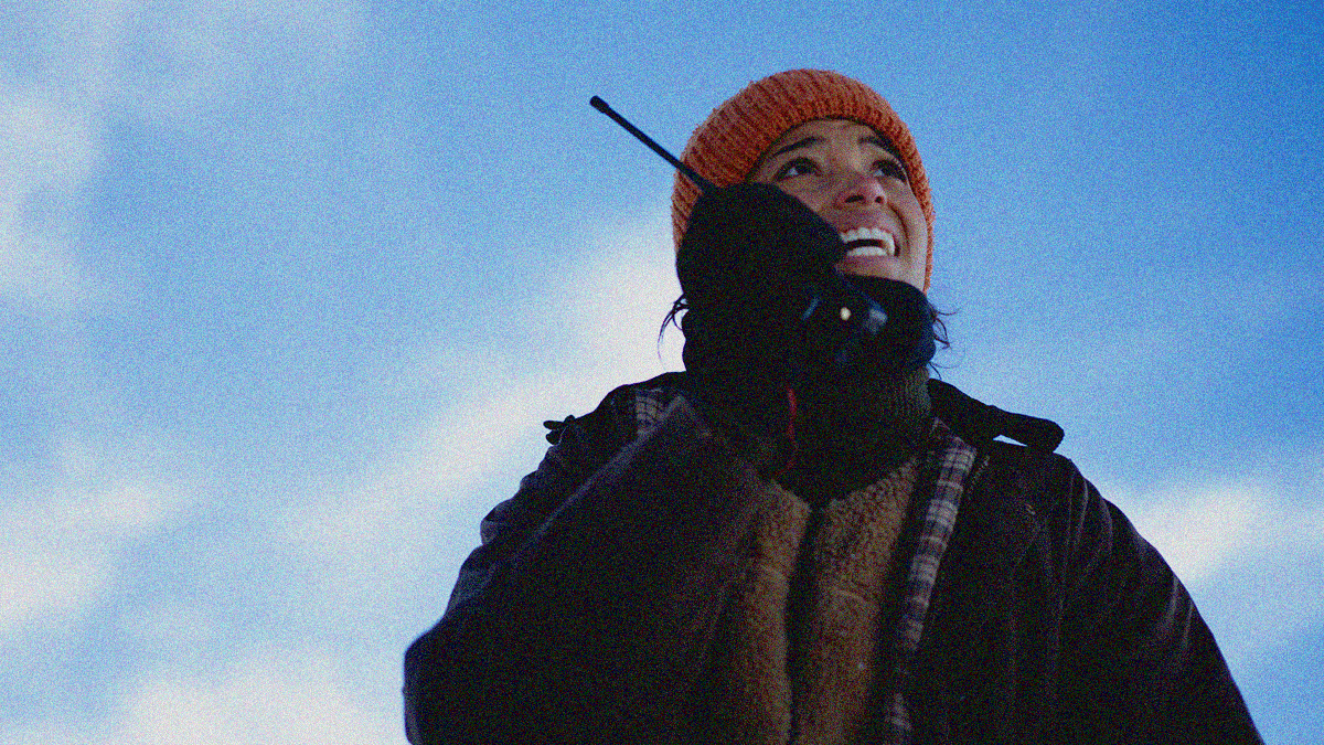 A woman in winter jacket and hat looks up into the sky while screaming into a walkie-talkie.