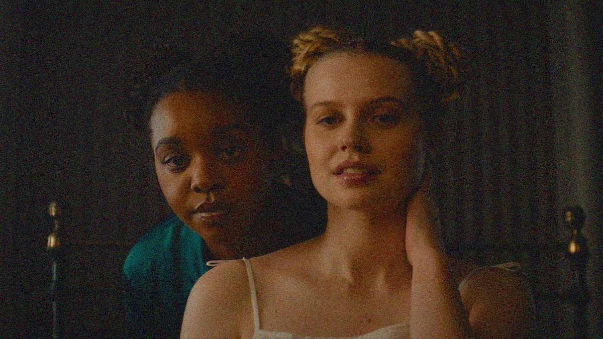 A Black woman stands behind a white woman as they both peer into the lens like a mirror.