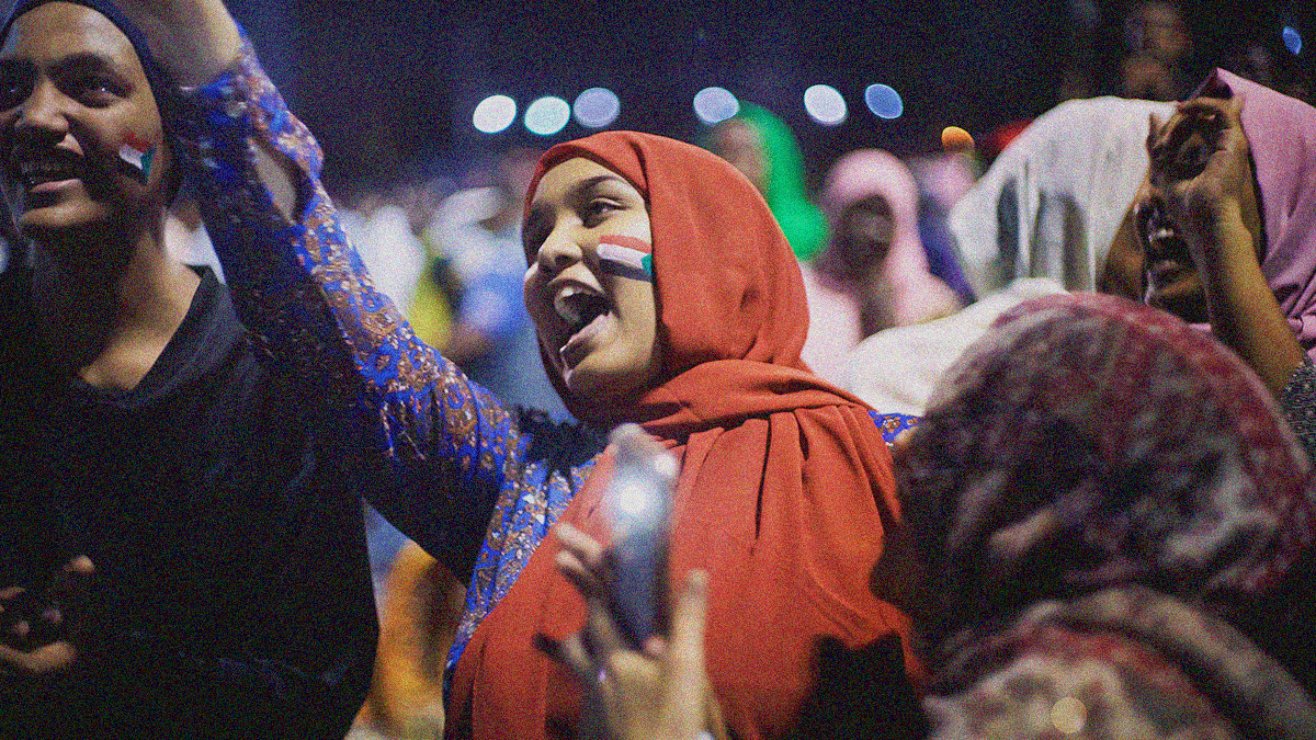 A protestor in a red hijab yells joyfully with a crowd.