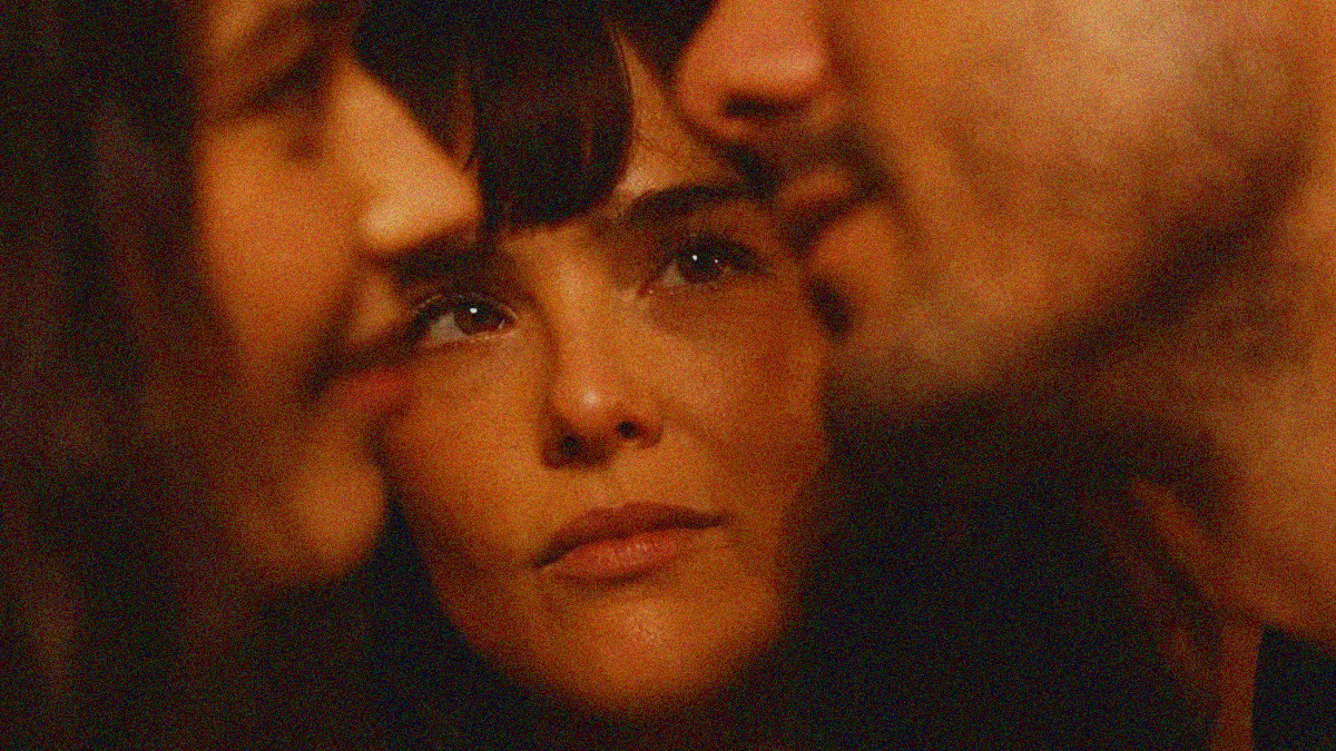 A woman's face is seen gazing at he face of a man about to kiss another woman—the latter two faces coming in through the sides in the foreground to frame her.