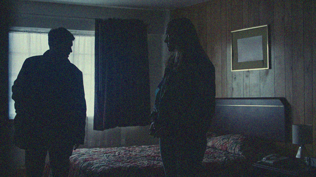 A man and a woman stand in a dark hotel room.