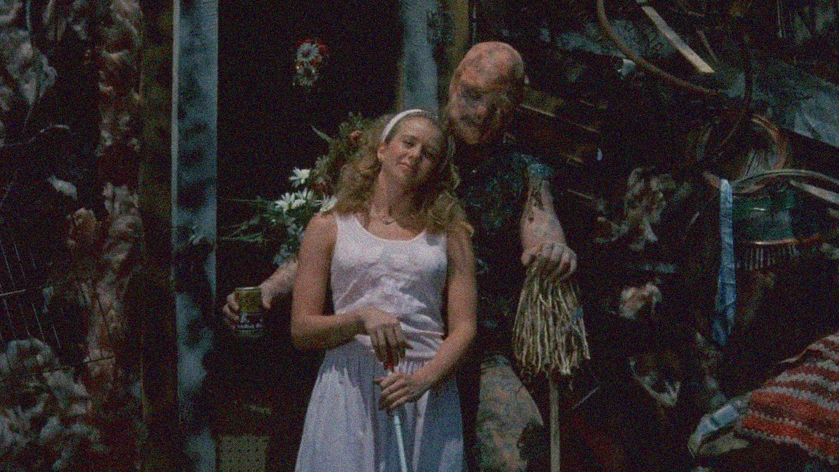 A woman in white leans happily against a radioactively disfigured man. Her hand is propped on a white cane for the blind. His hand is propped on an overturned mop.