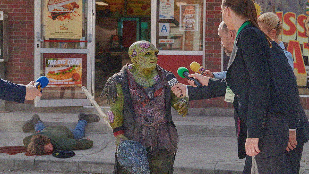 Toxie the radioactive mutant stands on the street with mop in hand as new reporters shove their microphones into his face. A dead body can be seen on the sidewalk behind them.