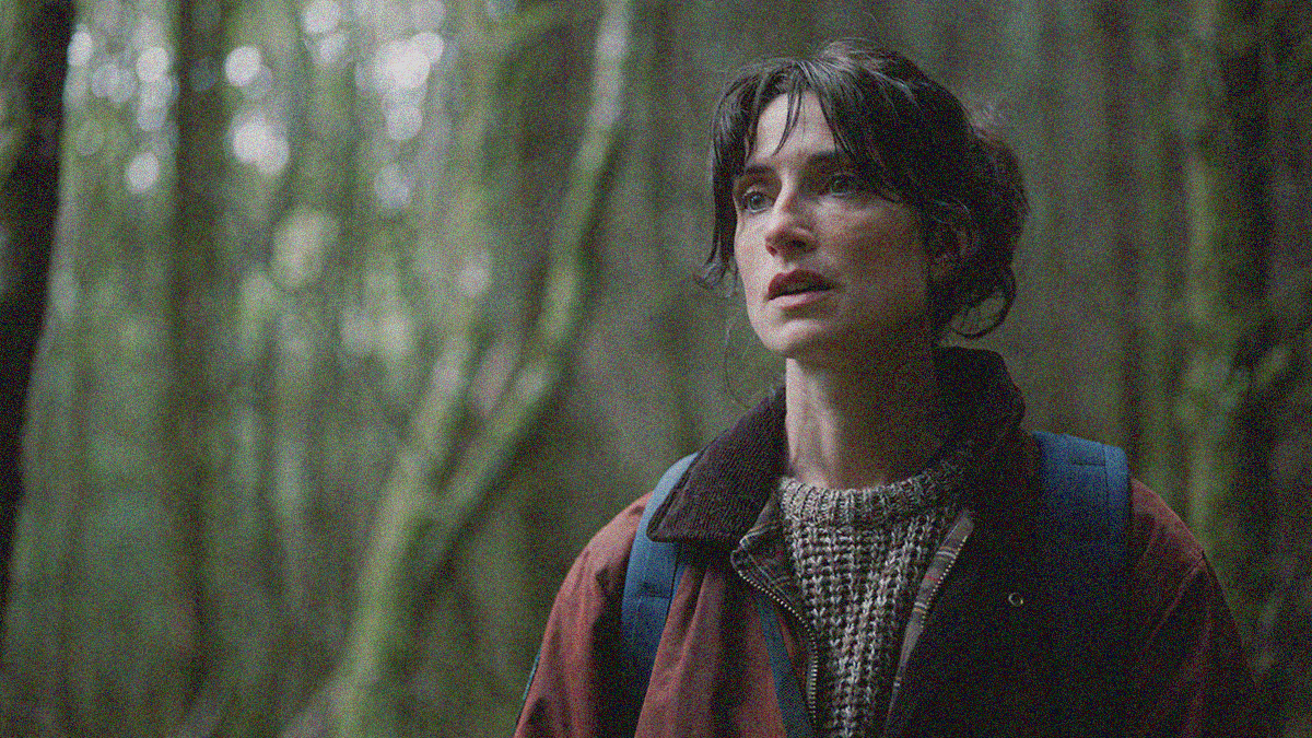 A woman taking up the right half of the frame looks off the page with mouth agape, a forest of trees fills up the rest of the space.