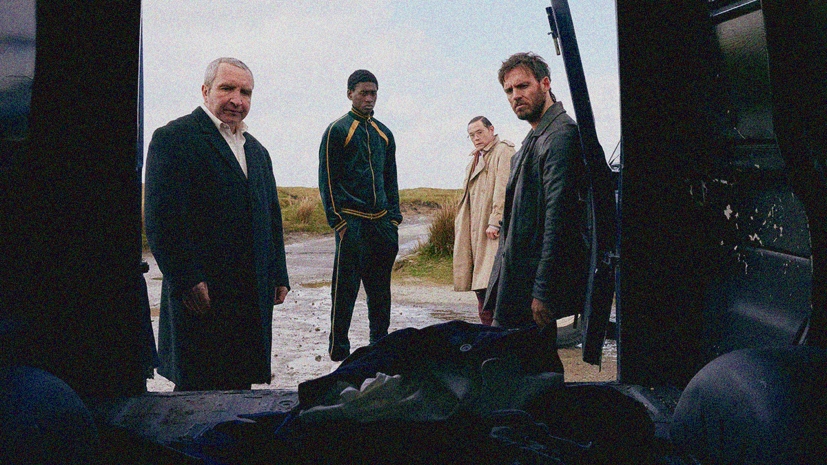 Four men peer at a pile of clothes on the floor of a van from which our vantage is inside looking out the open back door at them.