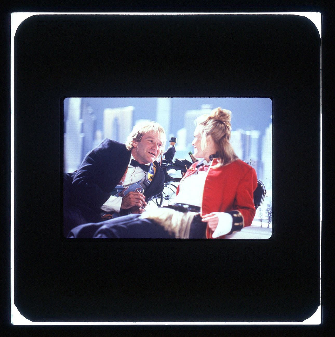 Robin Williams in black tux and Robin Wright in red soldier's jacket leaning back in repose while talking.