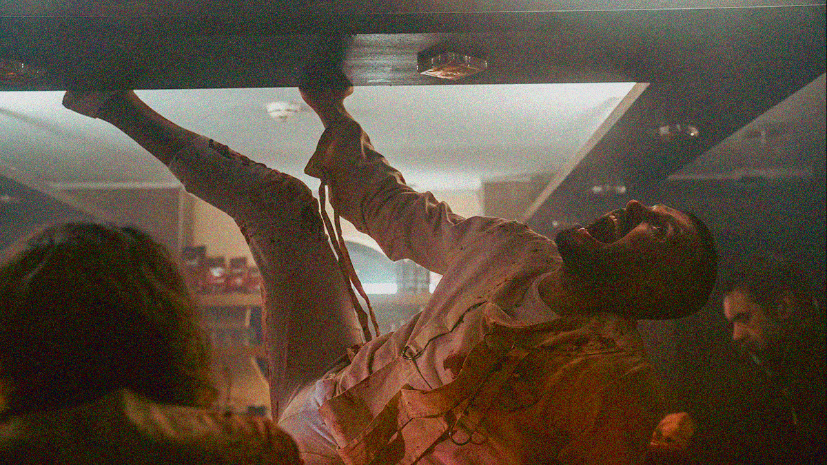 A man in a straitjacket screams while covered in blood and hanging from an overhang in the ceiling.