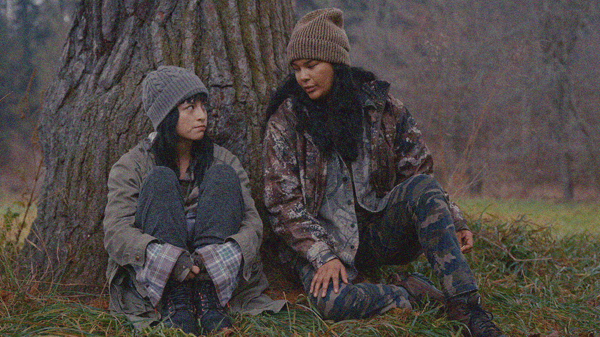 Two women sit in the grass against a tree.