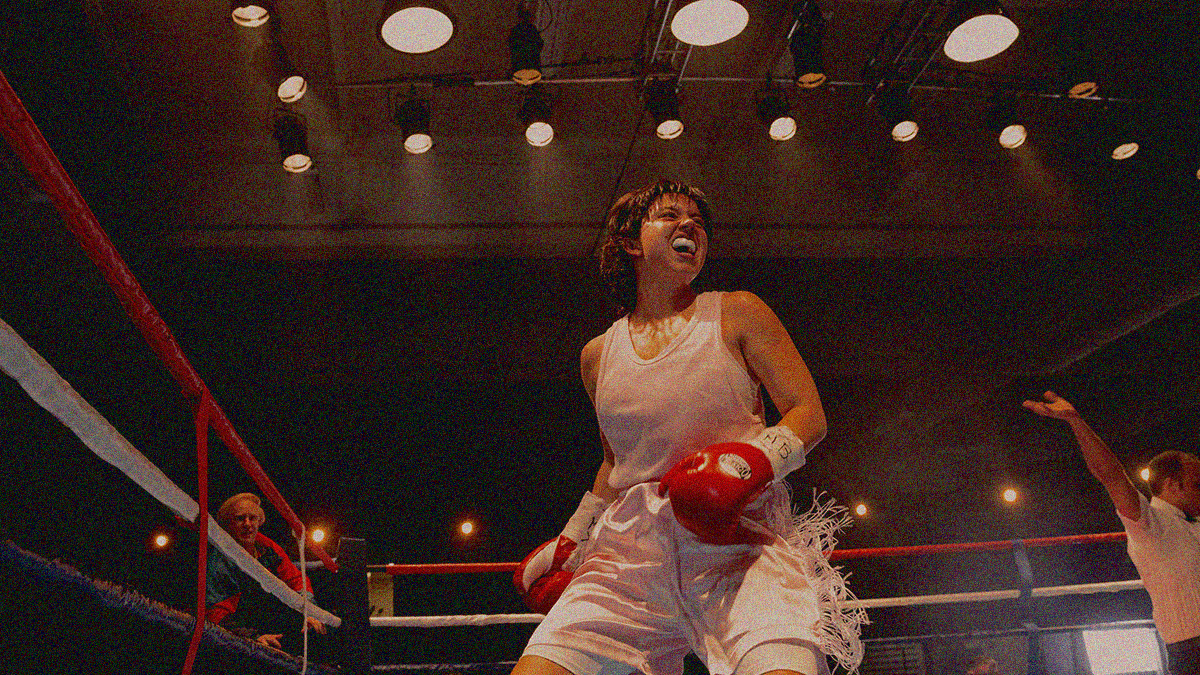 A woman boxer in pink is centered in the frame and shot from below yelling in excitement within a boxing ring..