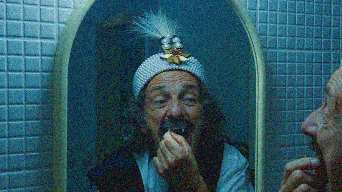A man dressed as Vlad the Impaler looks into a mirror and touches a fang.