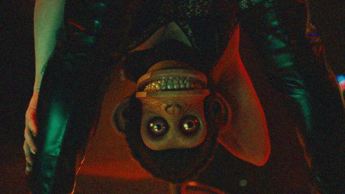 Freeze frame from a hallucination where a stripper bends to show her face between her legs, but her face is the grinning monkey face from the wind-up "toy."
