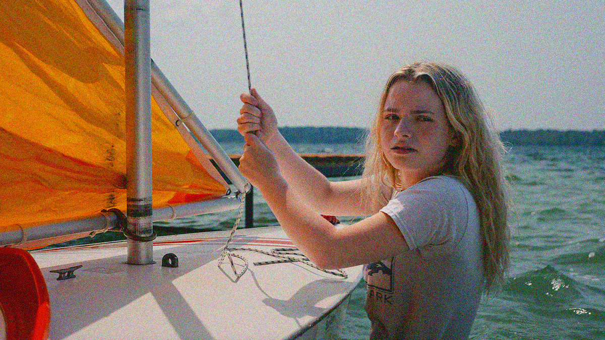 Close-up of a teenage girl looking off-screen while pulling the rope line to extend the sail of her Sunfish sailing dinghy.