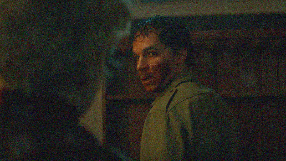 A man with blood covering his cheek turns to look over his shoulder at a woman in the foreground.