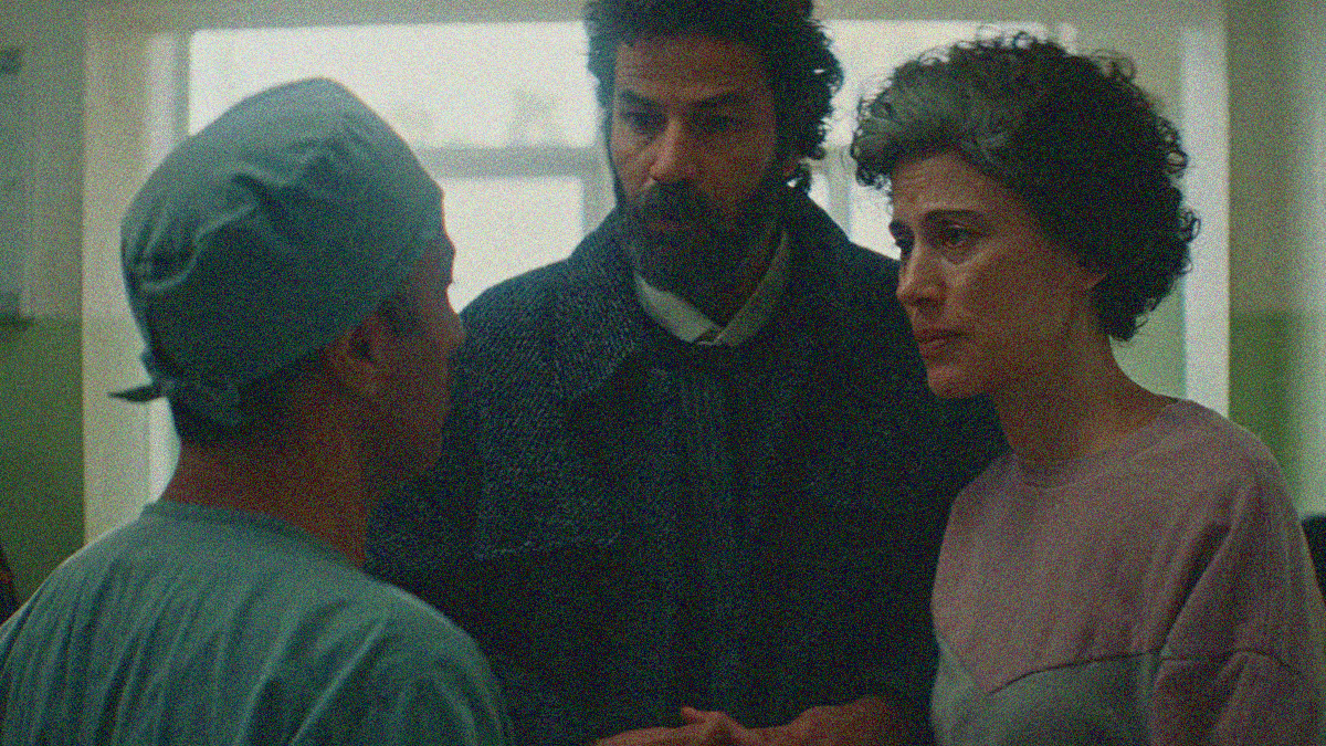 A bearded man and a graying-haired woman listen as a doctor in scrubs delivers them news.