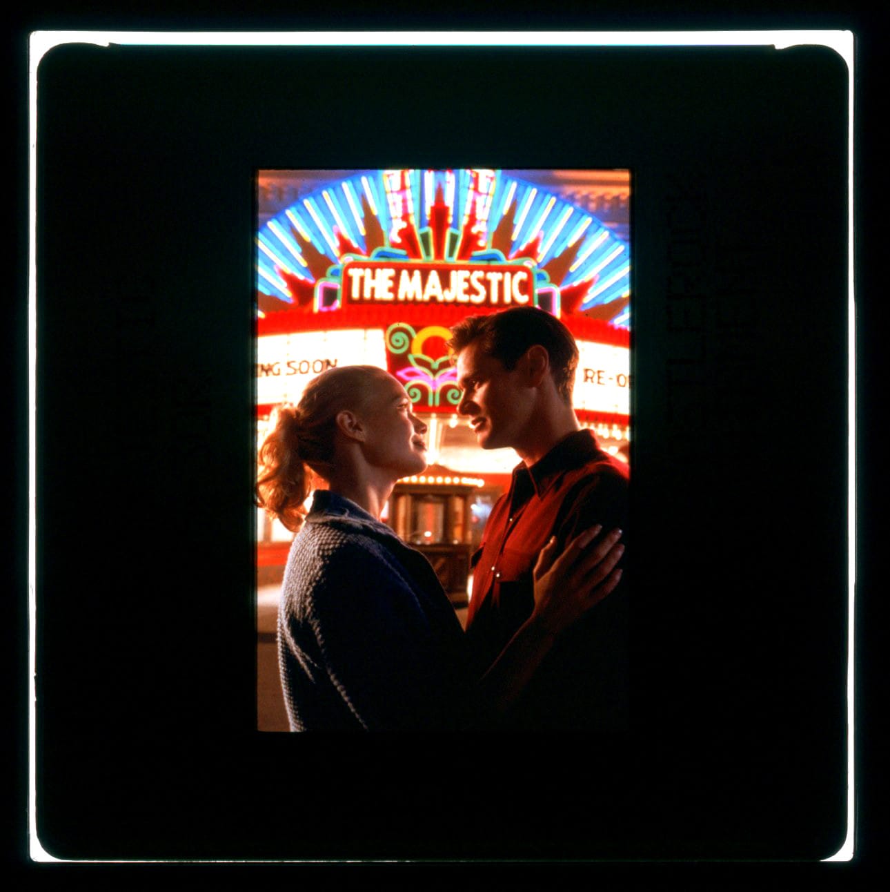 Color Publicity slide for THE MAJESTIC with a woman and man looking into each other's eyes while a colorful theater marquee is seen behind them.