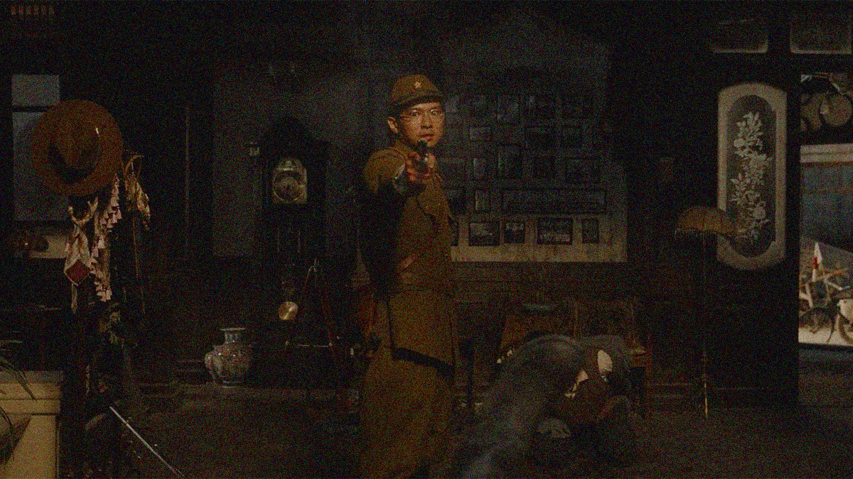 A Japanese soldier points a gun at the camera in a darkened room with a body on the floor by his side.