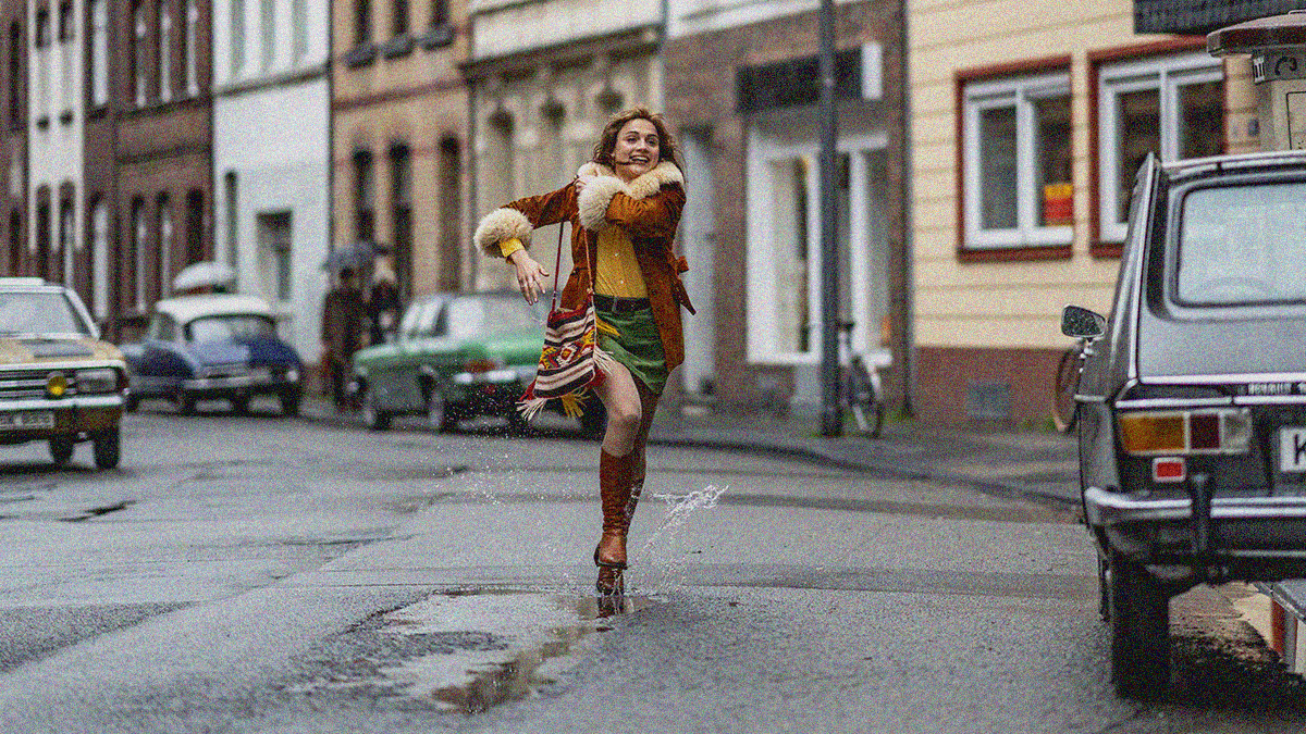 A young woman is center frame running down the middle of a street with a smile on her face.
