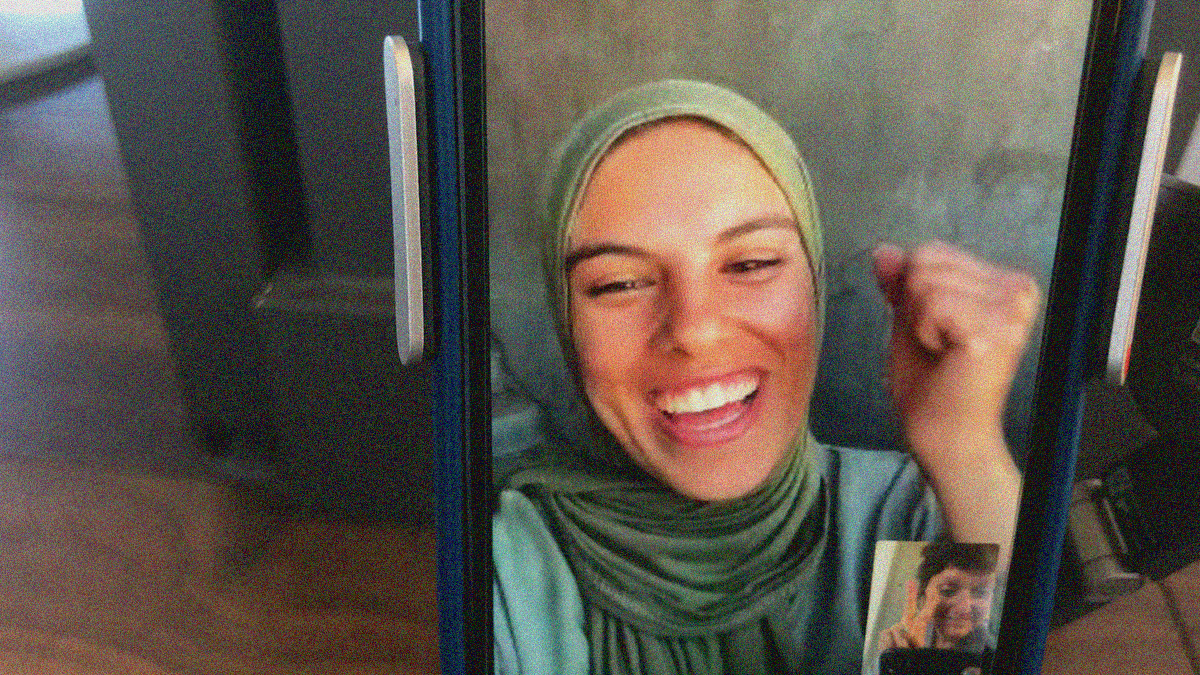 Close-up of a cellphone screen with a woman in hijab laughing as another is seen in a smaller window in corner of screen.
