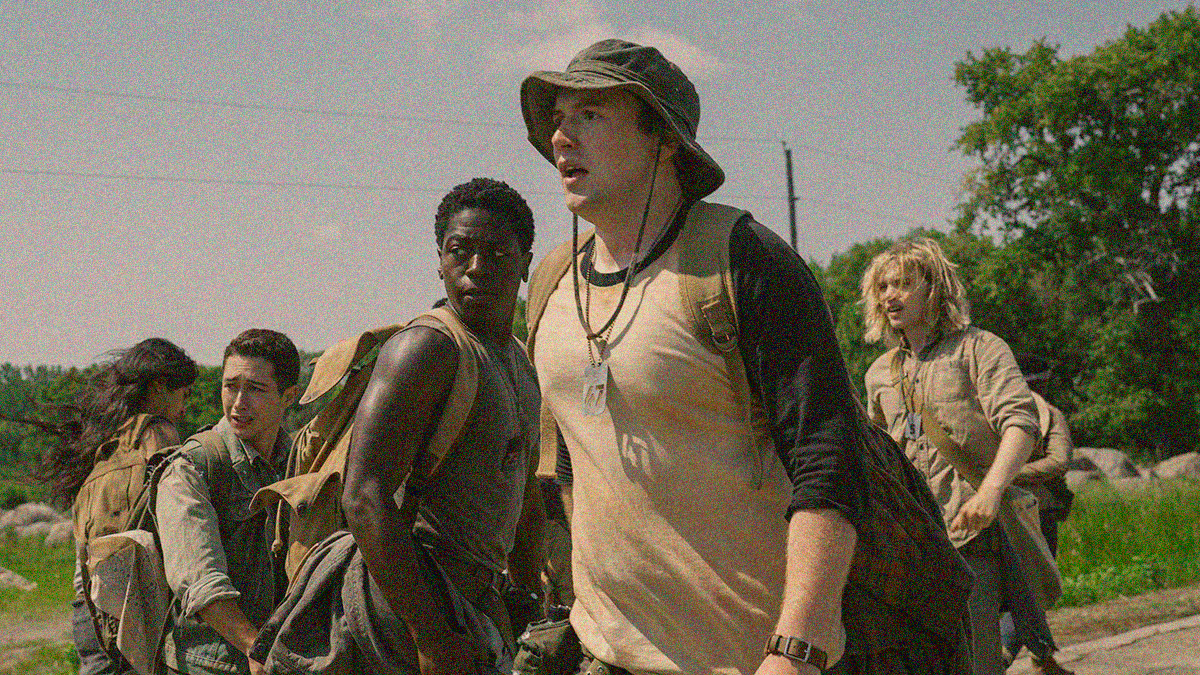 A group of men on a road, most of them look back off-screen left in horror.