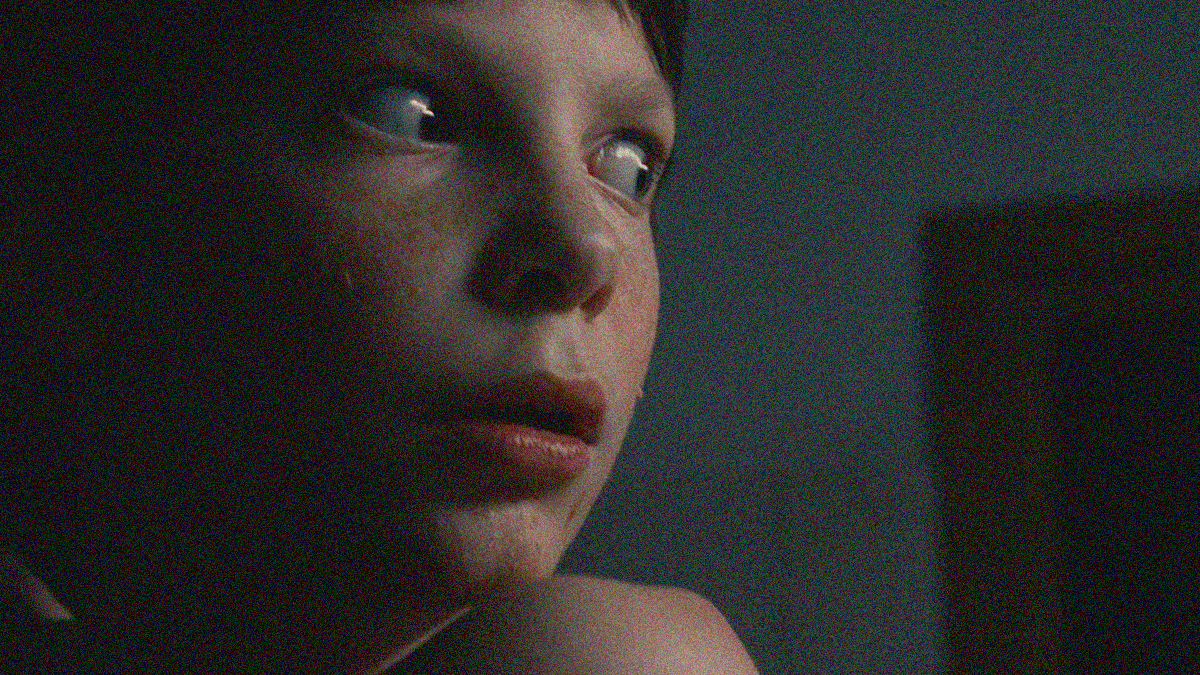 Close-up of a young boy looking wide-eyed and scared as he peers right.