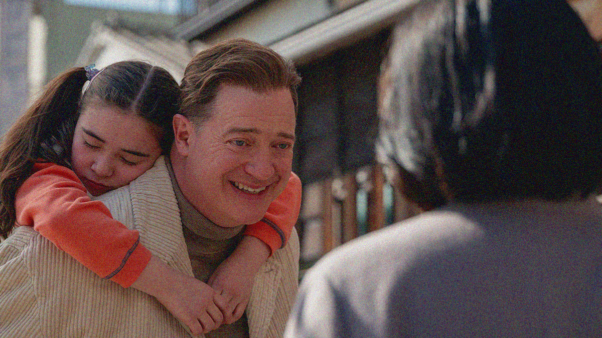 A young girl hangs in an embrace with eyes closed on the shoulder of a man. He smiles at a woman shown from behind in the foreground.