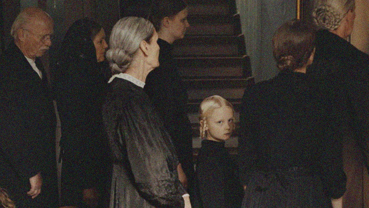 A line of adults in black face right while a young blonde girl turns and looks into the camera.