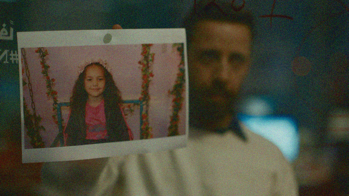 A man blurred in shallow focus holds up a photograph of a smiling young girl.