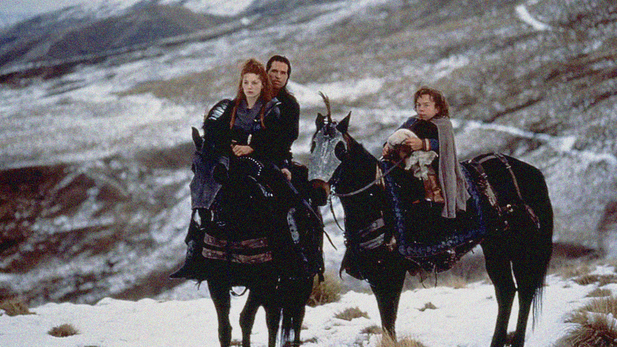 Two horses center frame. The left has a woman sitting in front of a man. The right has a man sitting with a swaddled baby in his lap.