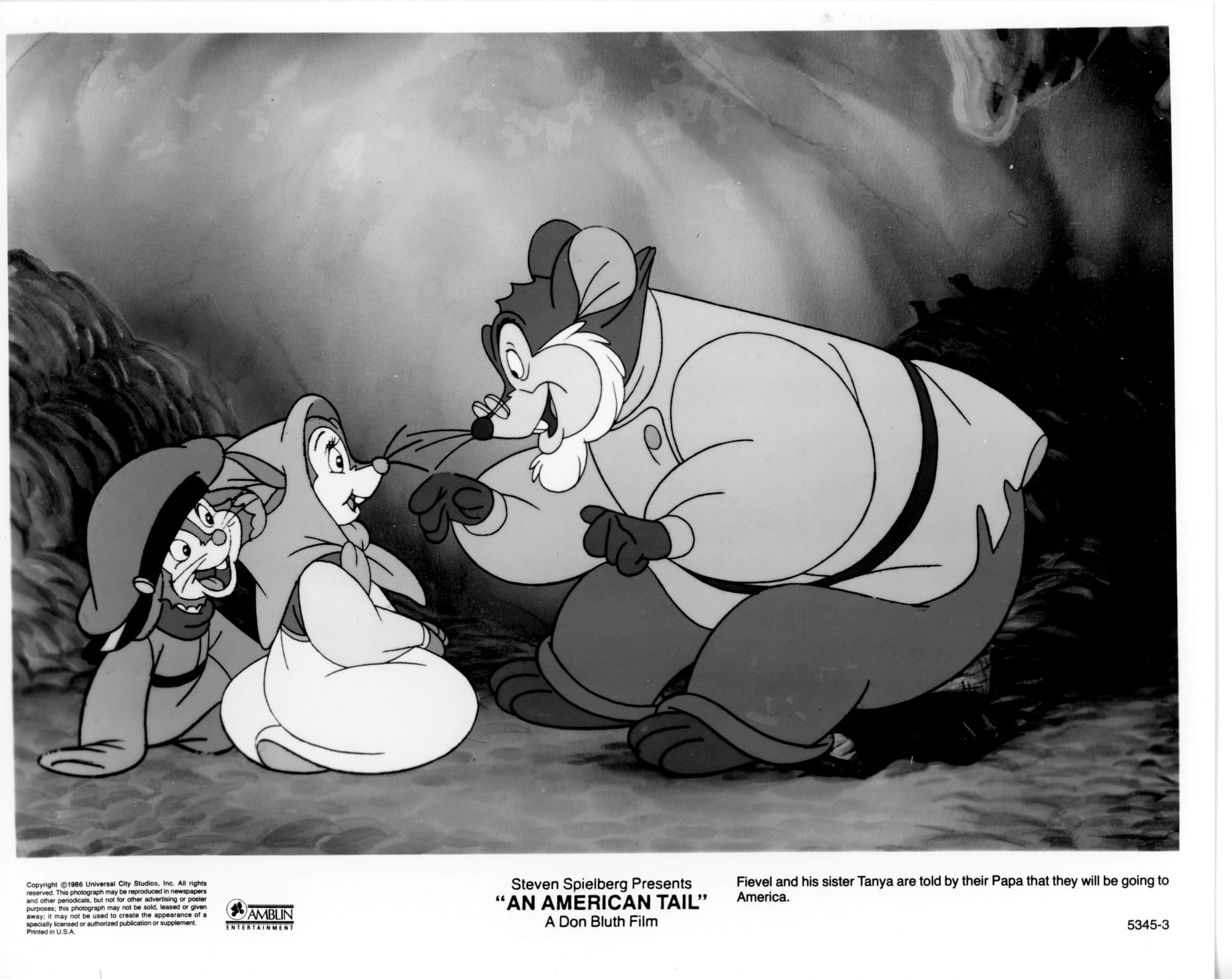 B&W Publicity Photo: An older mouse with glasses and white beard fills right half of frame, sitting and leaning over two children mice with a smile. One of the children is a boy with giant hat on head and the other is a girl with scarf tied around head.