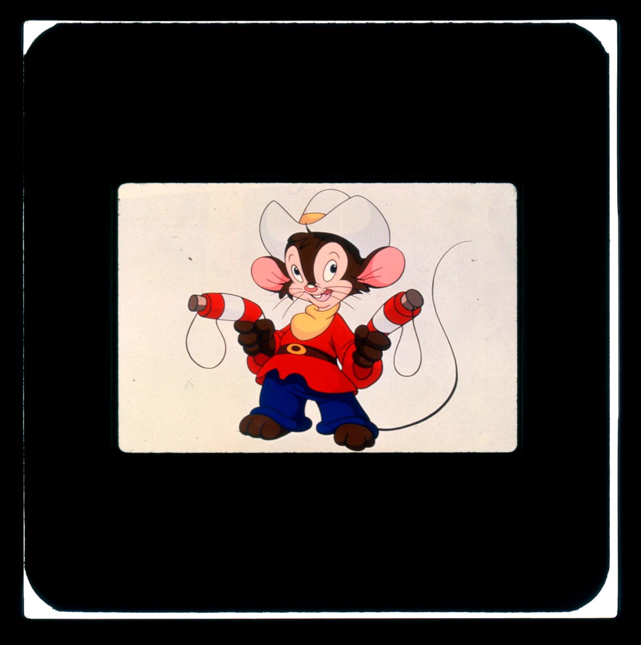 Color publicity slide of a young mouse in red shirt and blue paints wearing a cowboy hat. He has a gun in both hands (with strings attached to bottle cork "bullets") and he is fully masked out on a white background.