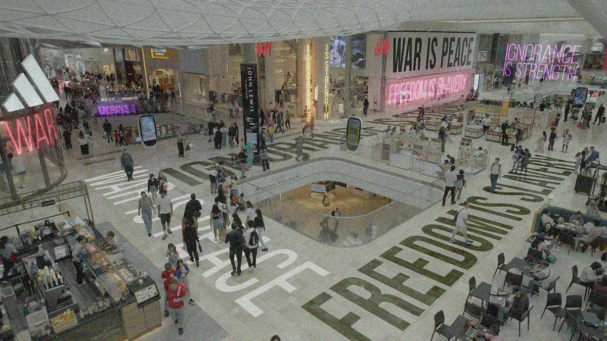 A wide view of a packed mall interior with the 1984 slogans "Freedom is slavery", "War is peace", and "Ignorance is strength" superimposed on the floor, walls, and neon signs.
