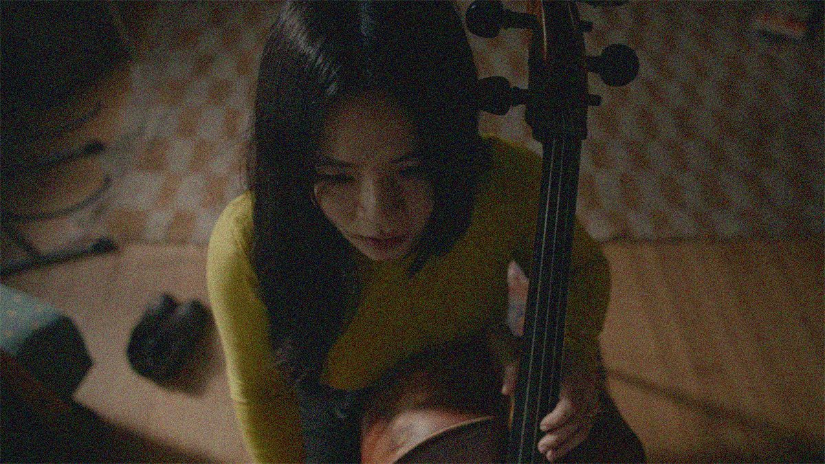 Camera is angled above a woman's head as she sits with cello in-hand to play.