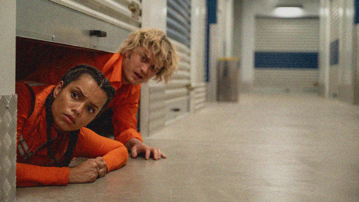 A woman and man pop their heads out from under an indoor storage unit door on the floor.