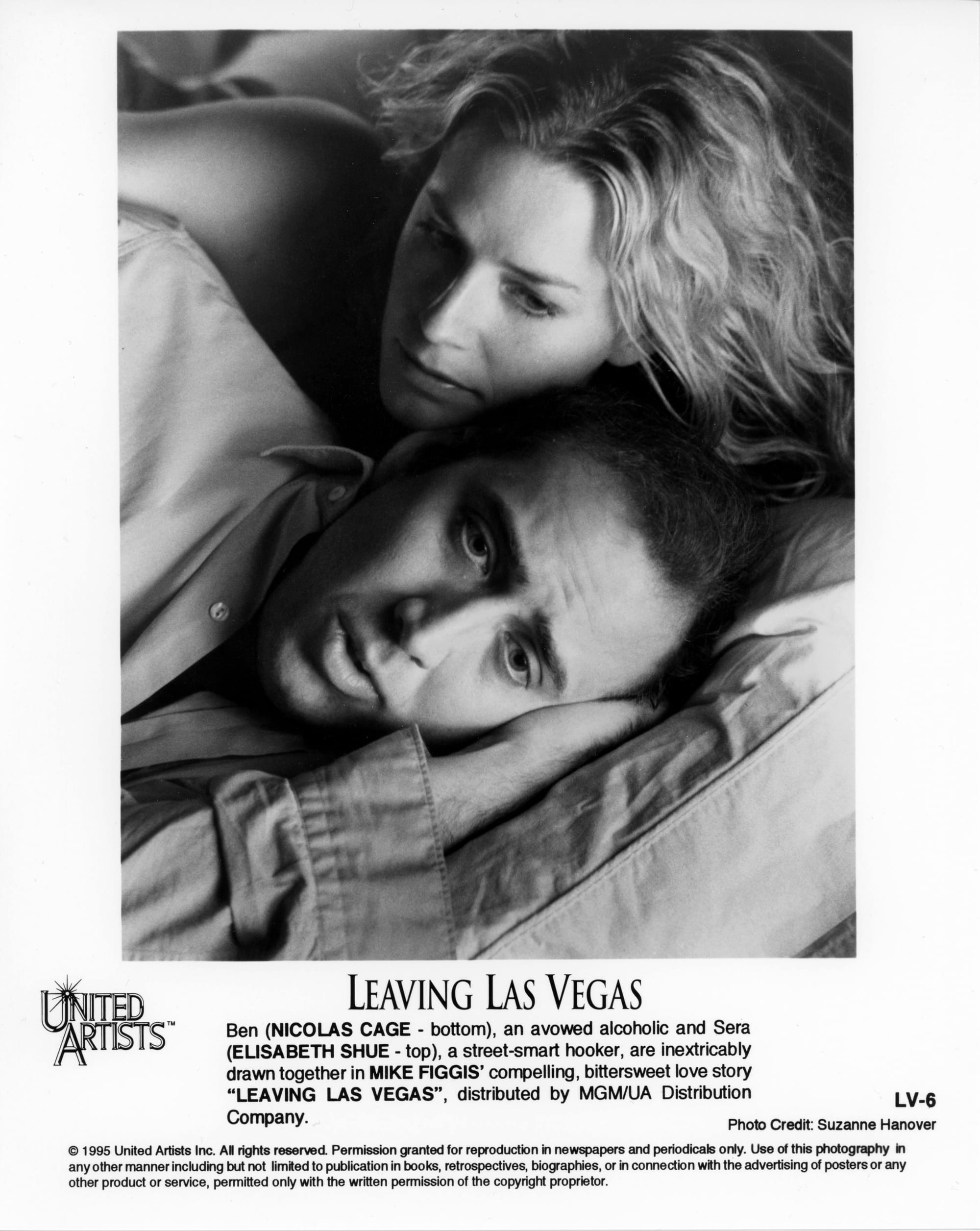 Close-up of two faces lying in bed. Man has head on hand on pillow while the woman can be seen above leaning over him.