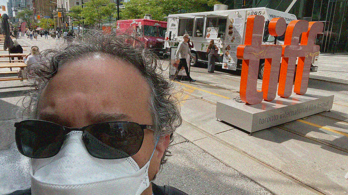 Selfie of me in sunglasses and an N95 with the TIFF logo street monument above my right shoulder.